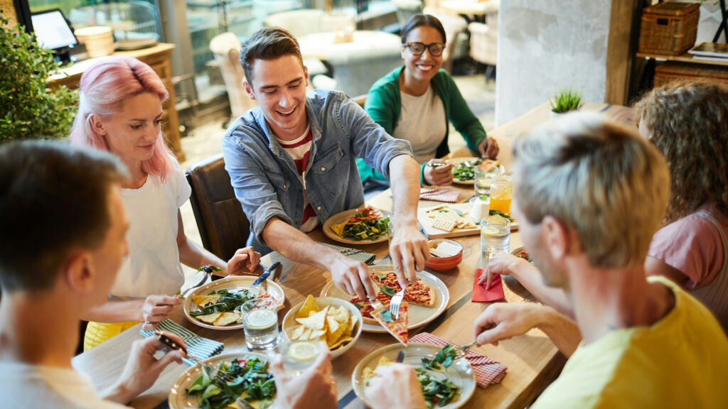 Eine Gruppe von Freunden lebt Gastfreundschaft indem sie ausgelassen zusammen Pizza essen